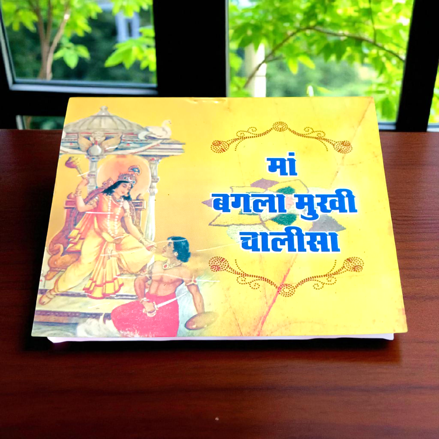 A book titled "Baglamukhi Chalisa" in Hindi with a picture of Maa Baglamukhi’s idol, placed on a divine altar with flowers and incense.