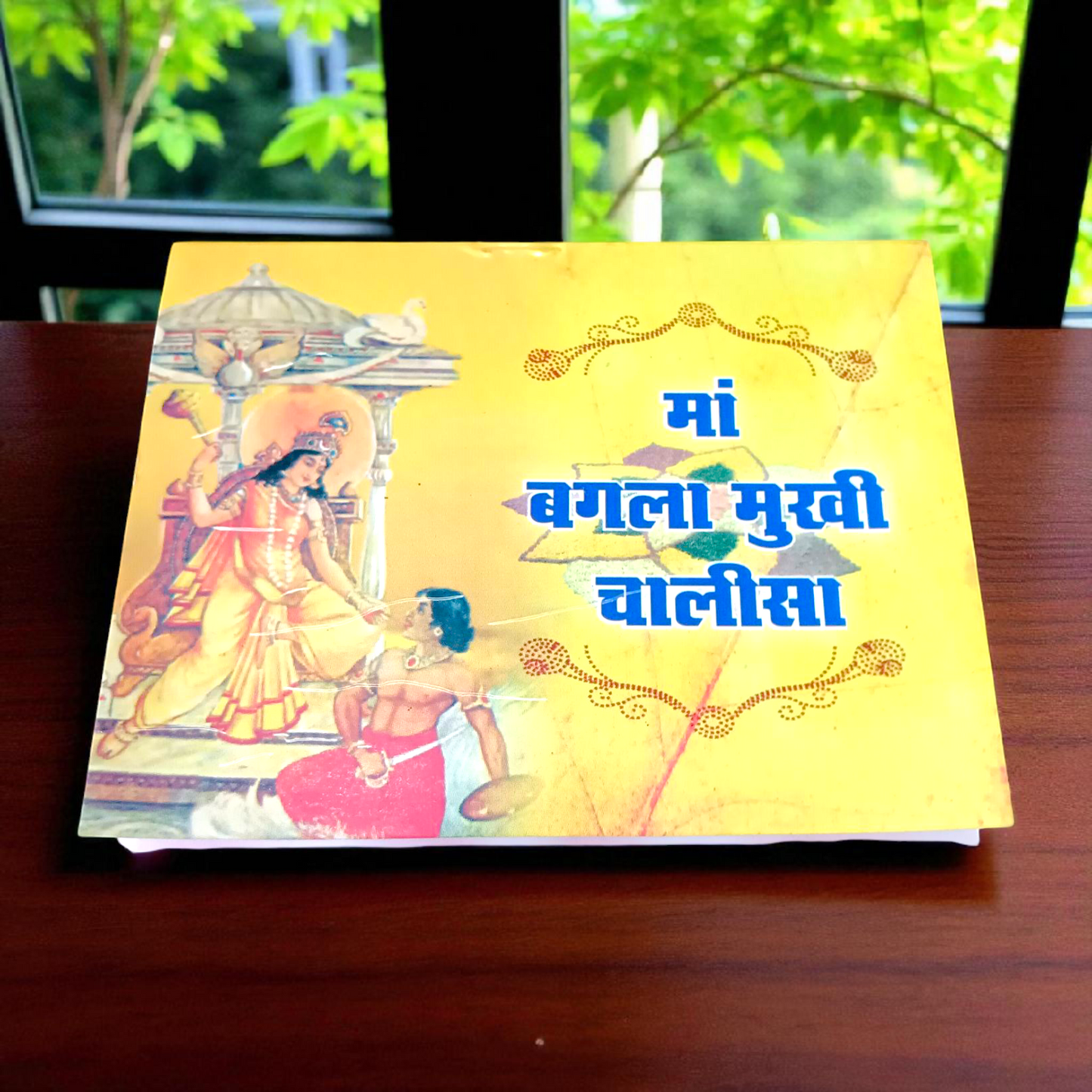 A book titled "Baglamukhi Chalisa" in Hindi with a picture of Maa Baglamukhi’s idol, placed on a divine altar with flowers and incense.