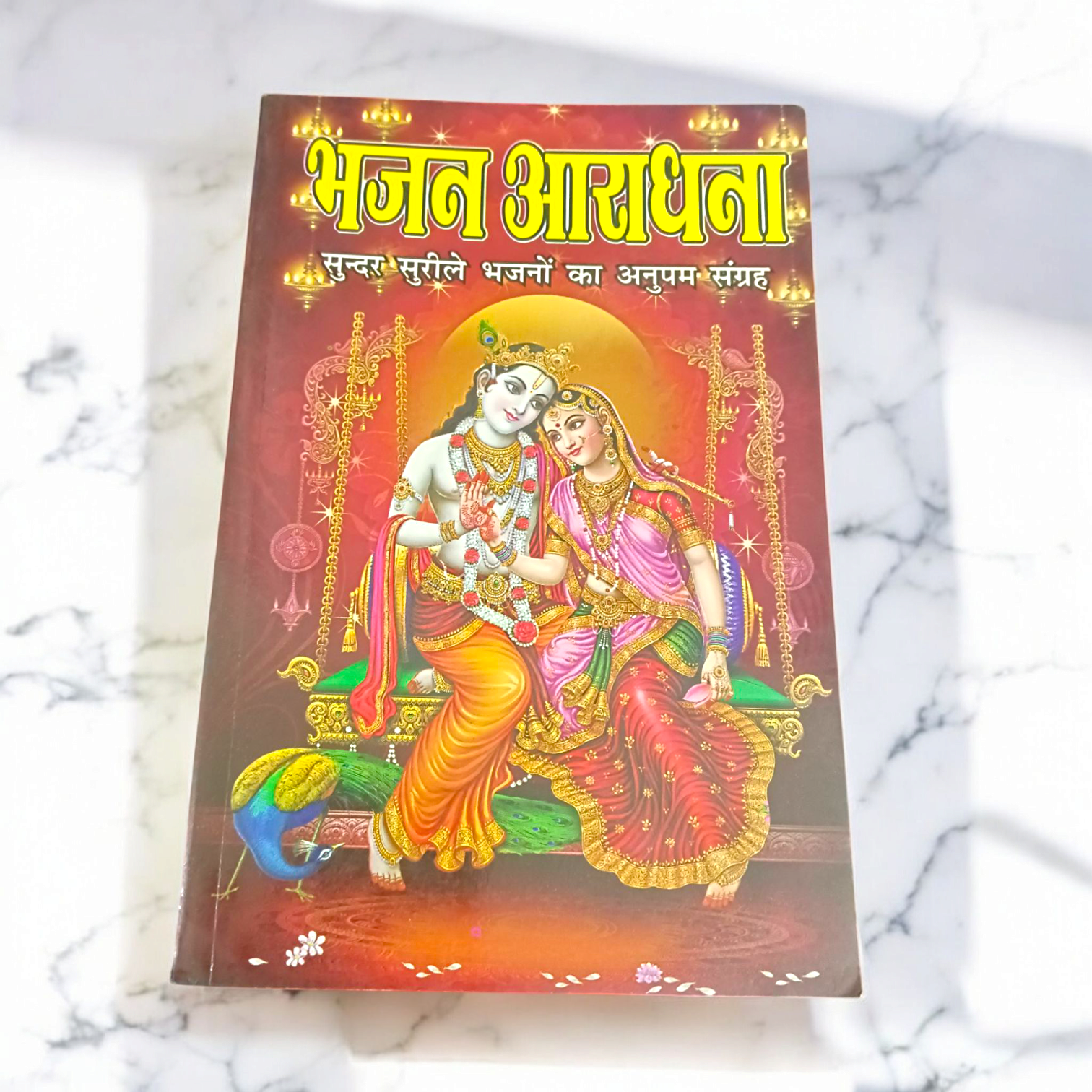A close-up of a Bhajan Book In Hindi featuring 200+ bhajans and 15+ aartis, with a peaceful spiritual background.