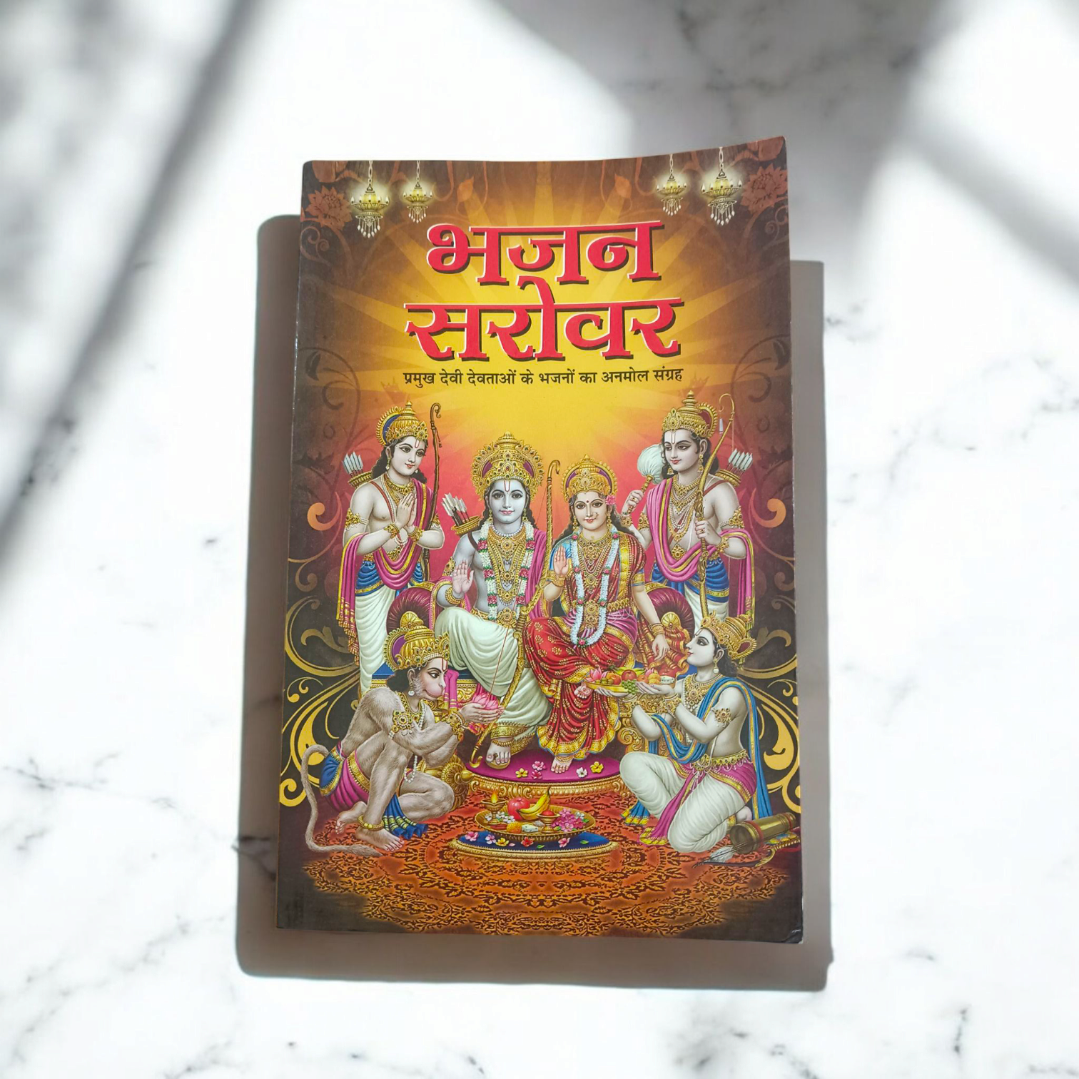 A person holding a Bhajan Book In Hindi featuring devotional bhajans and aartis, with a serene background of a temple.