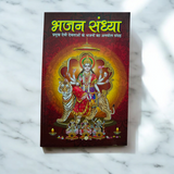 A person holding a Bhajan Book In Hindi featuring devotional bhajans and aartis, with a serene background of a temple.