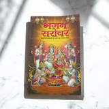 A person holding a Bhajan Book In Hindi featuring devotional bhajans and aartis, with a serene background of a temple.