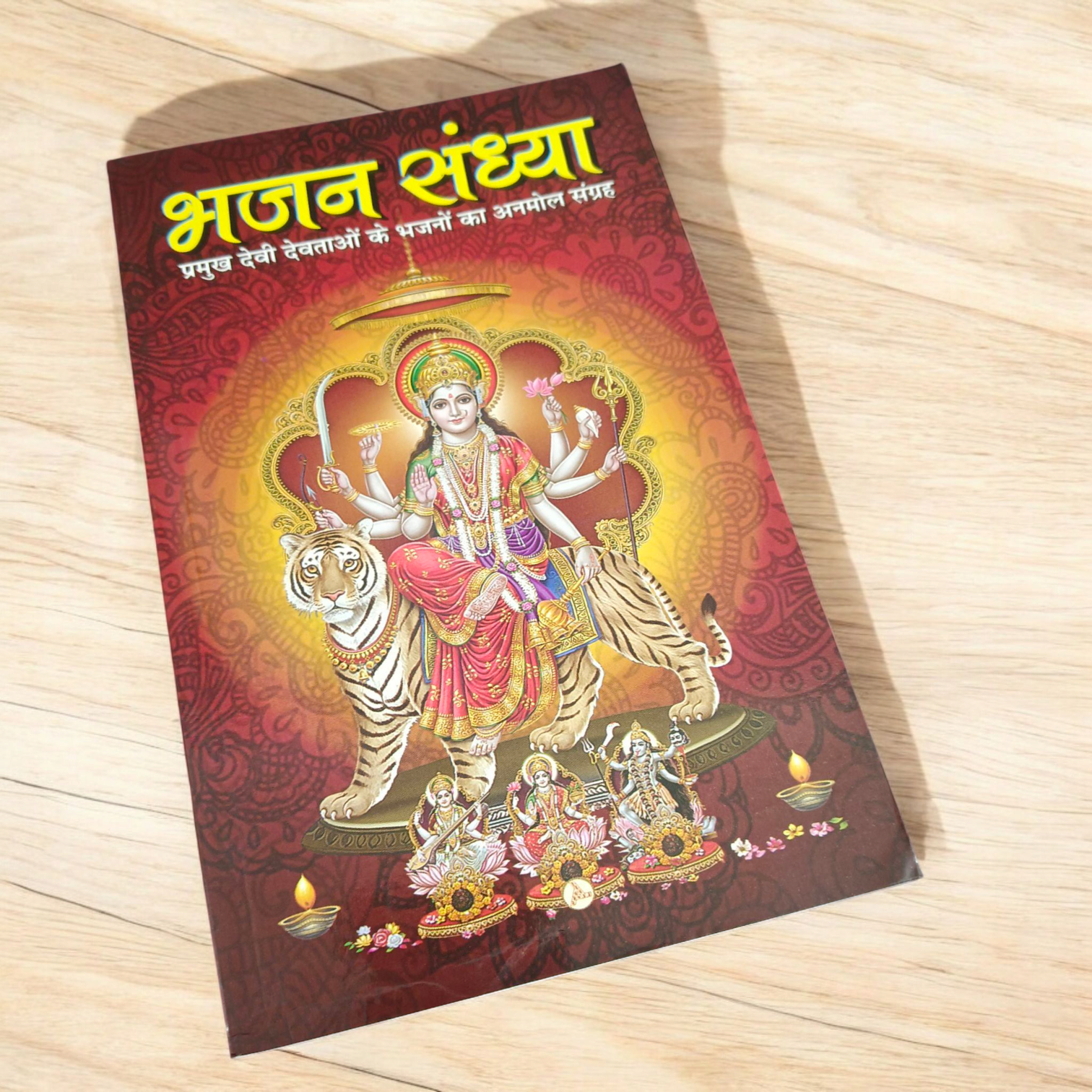 A person holding a Bhajan Book In Hindi featuring devotional bhajans and aartis, with a serene background of a temple.