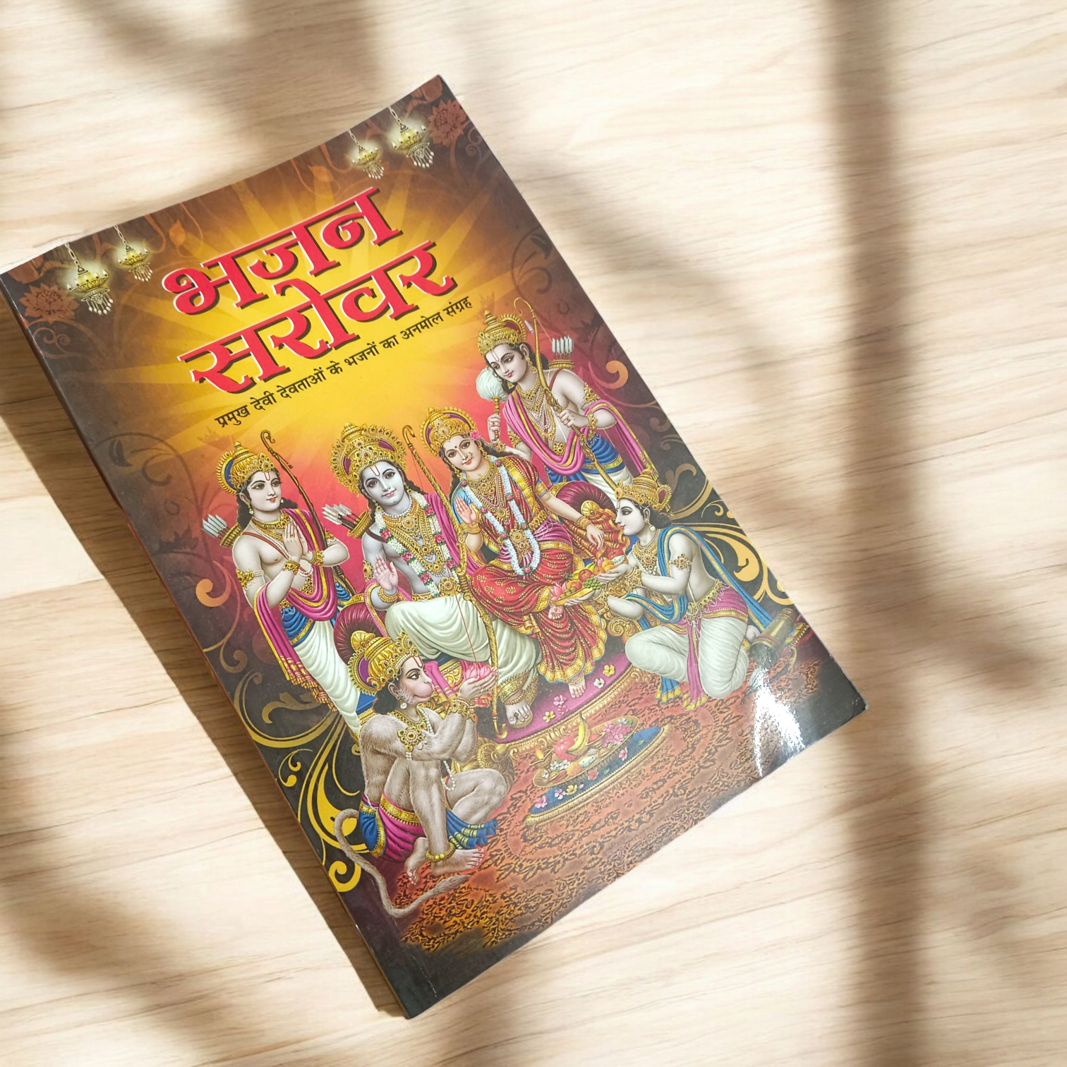 A person holding a Bhajan Book In Hindi featuring devotional bhajans and aartis, with a serene background of a temple.