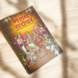 A person holding a Bhajan Book In Hindi featuring devotional bhajans and aartis, with a serene background of a temple.