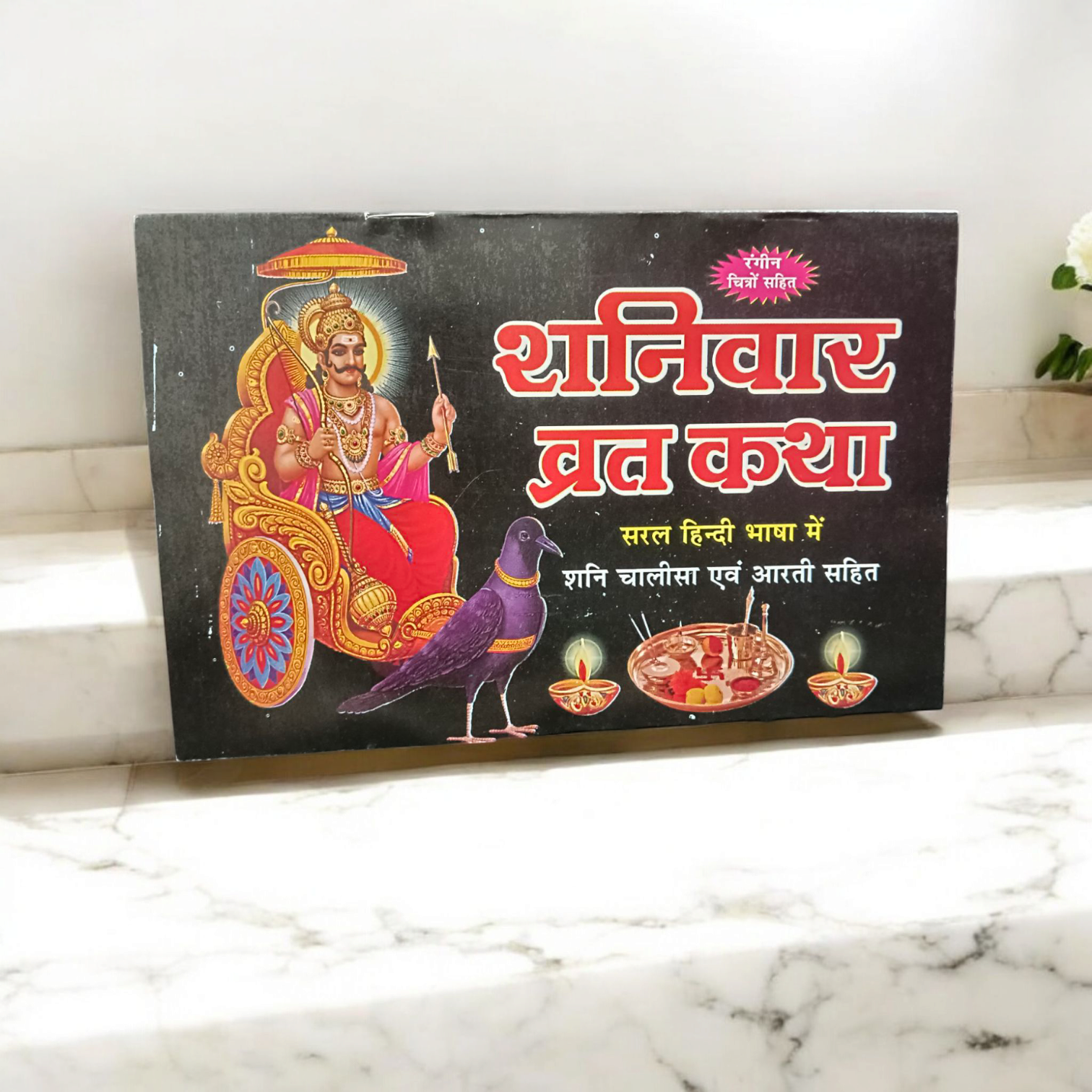 The Shaniwar Vrat Katha book, with an image of Lord Shani and symbols representing the planet Saturn, surrounded by spiritual motifs and prayer beads.