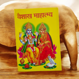 The image shows the cover of the Vaishak Mahatmya | Hindi Book, featuring detailed illustrations and symbols related to Hindu rituals and Vaishak month observances.