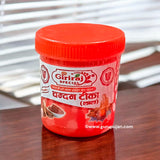 Three small containers of white, yellow, and red Chandan Tilak paste with a spiritual backdrop showcasing sandalwood and diya