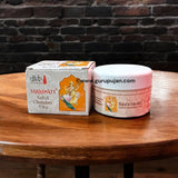 Three small containers of white, yellow, and red Chandan Tilak paste with a spiritual backdrop showcasing sandalwood and diya